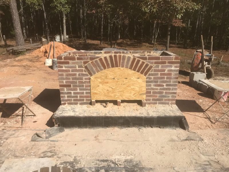 A brick fireplace is being built in the middle of a dirt field.