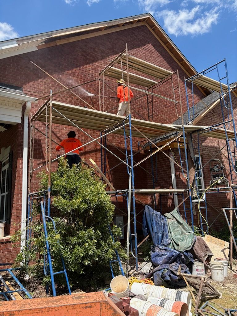A man is standing on a scaffolding in front of a brick building.