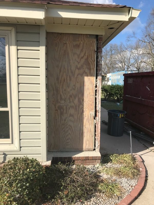 A house with a door boarded up and a dumpster in the background.