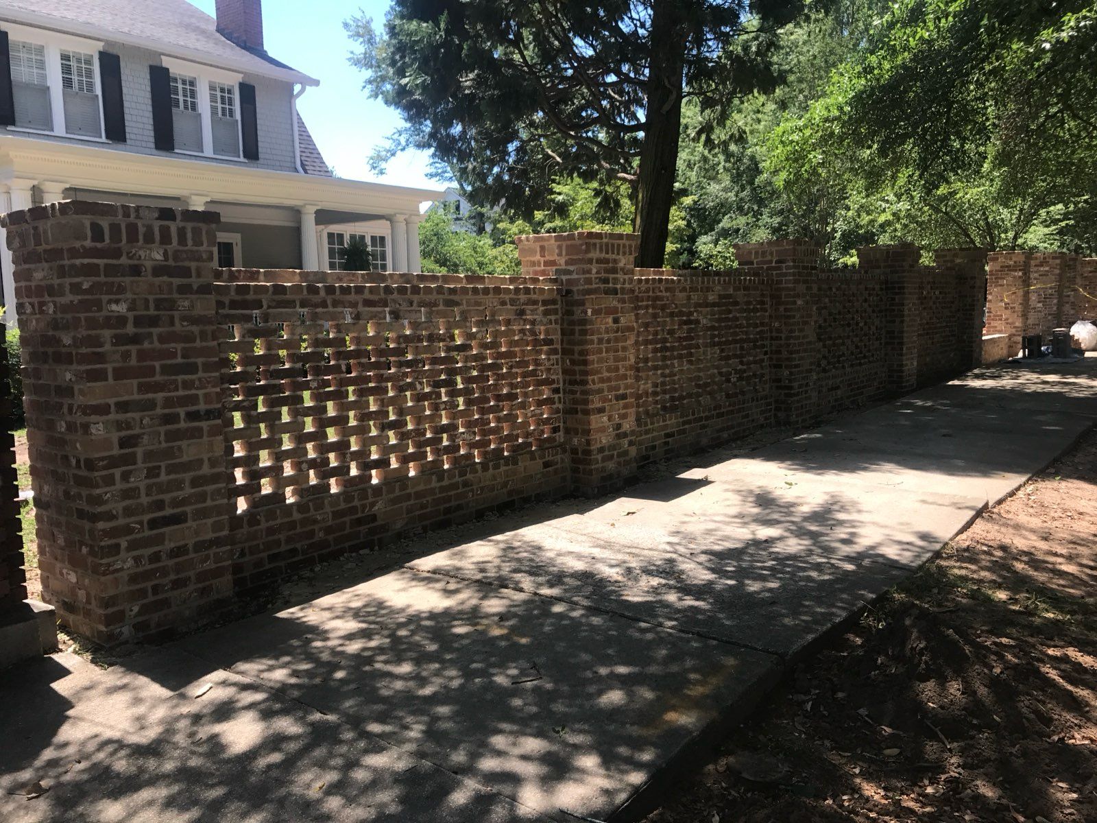A brick wall along a sidewalk in front of a house.