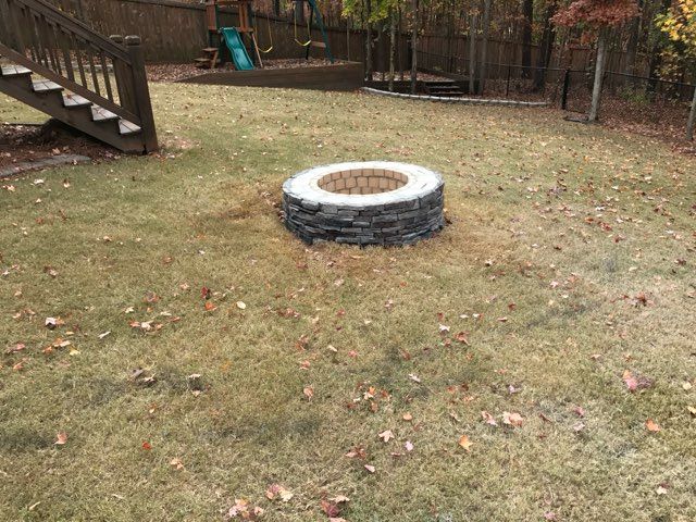 There is a fire pit in the middle of the grass in the backyard.
