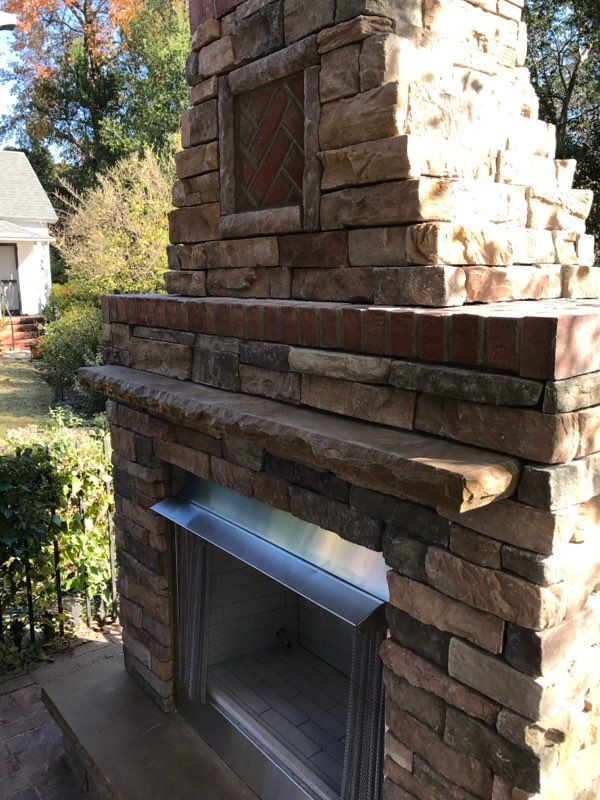 A brick fireplace with a stainless steel mantle is sitting in front of a house.