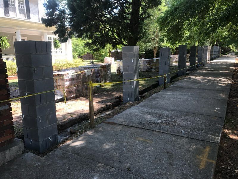 A brick fence is being built on the sidewalk in front of a house.