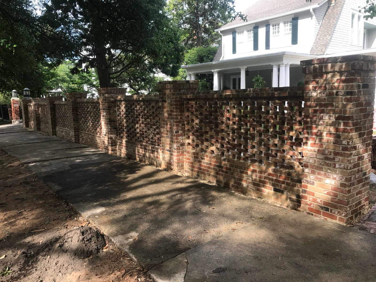 A brick wall surrounds a driveway in front of a house.