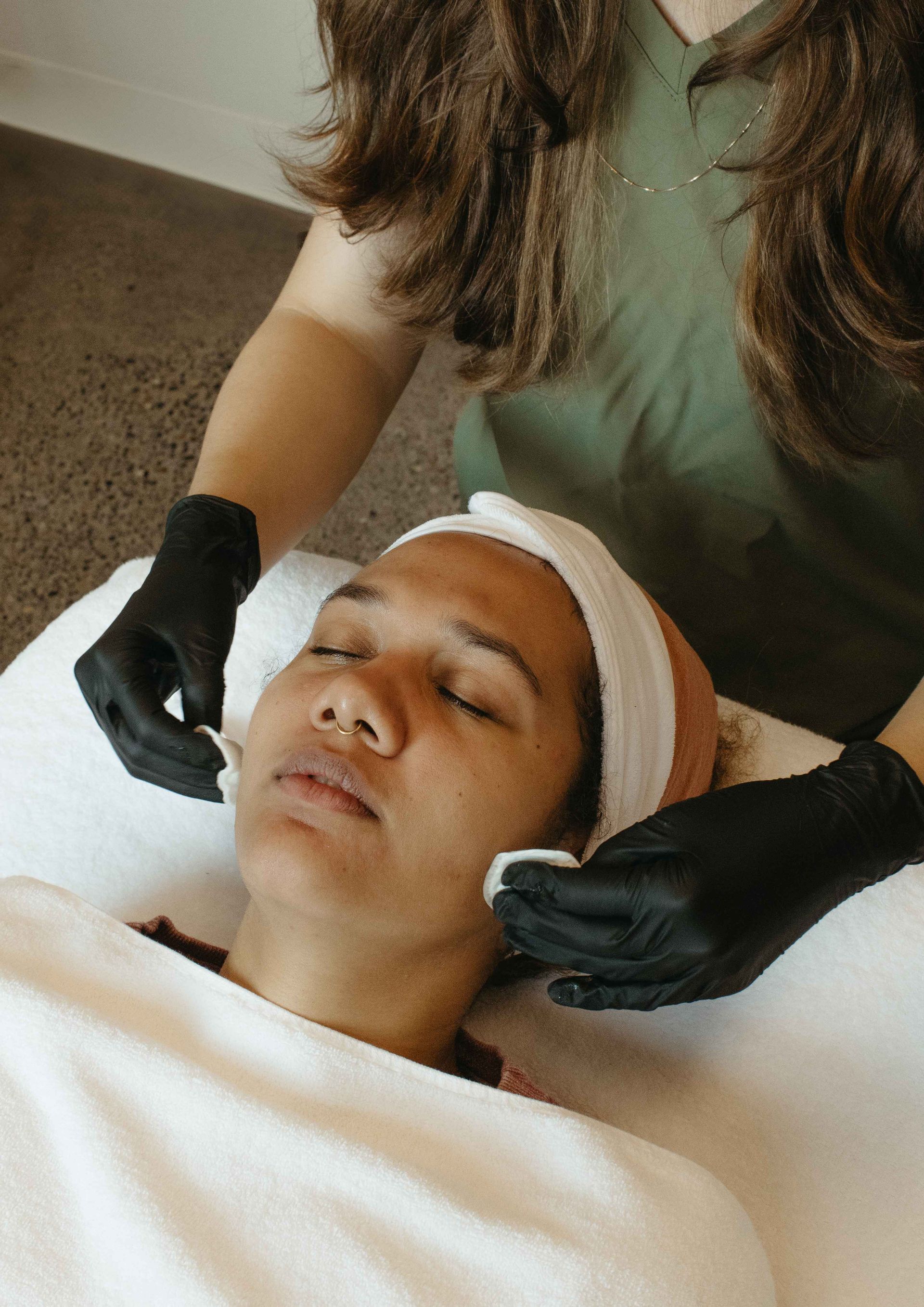 Person receiving facial treatment; esthetician applies product with cotton pads.