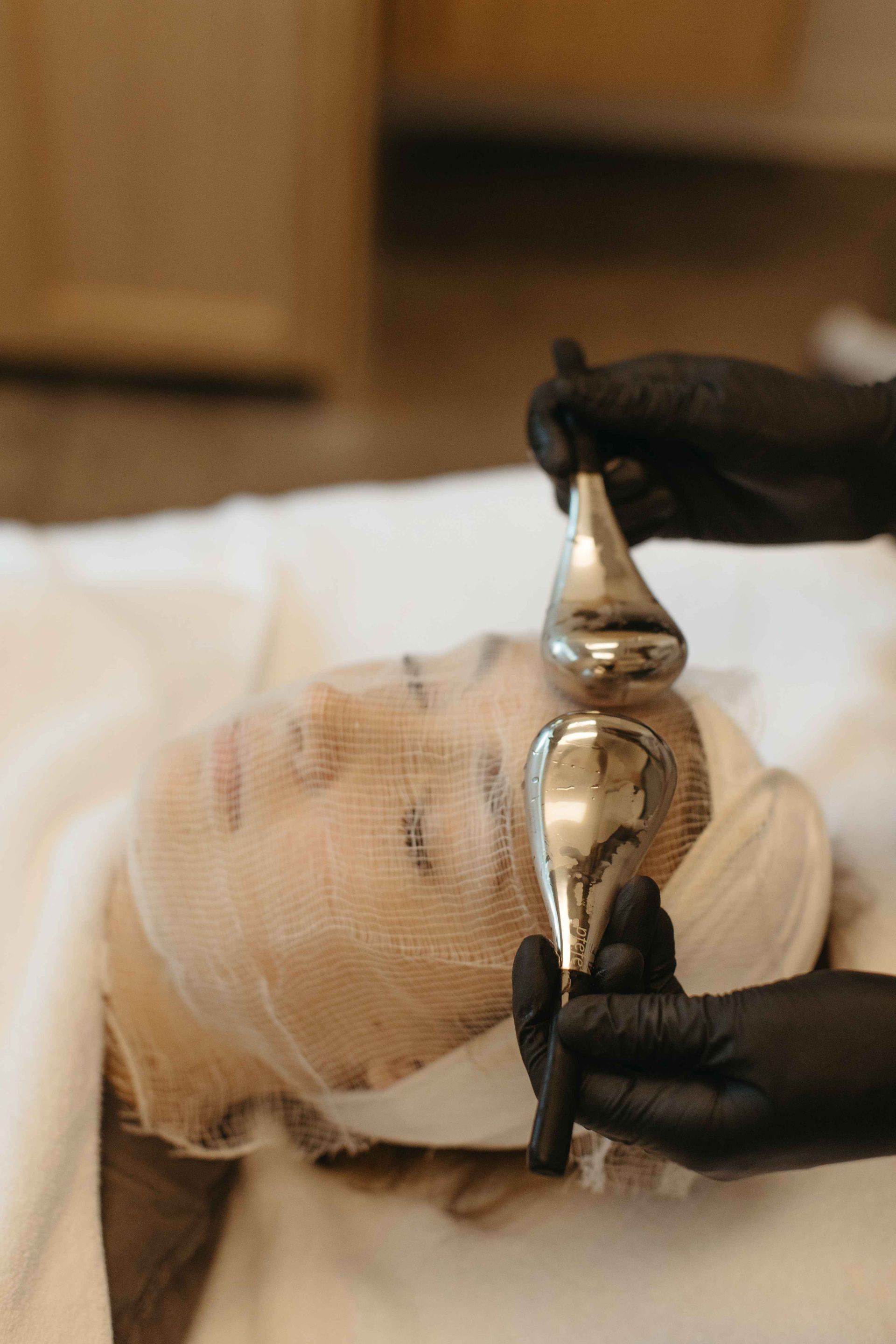 Woman receiving a facial treatment with silver tools. Hands in black gloves hold tools over face in spa setting.