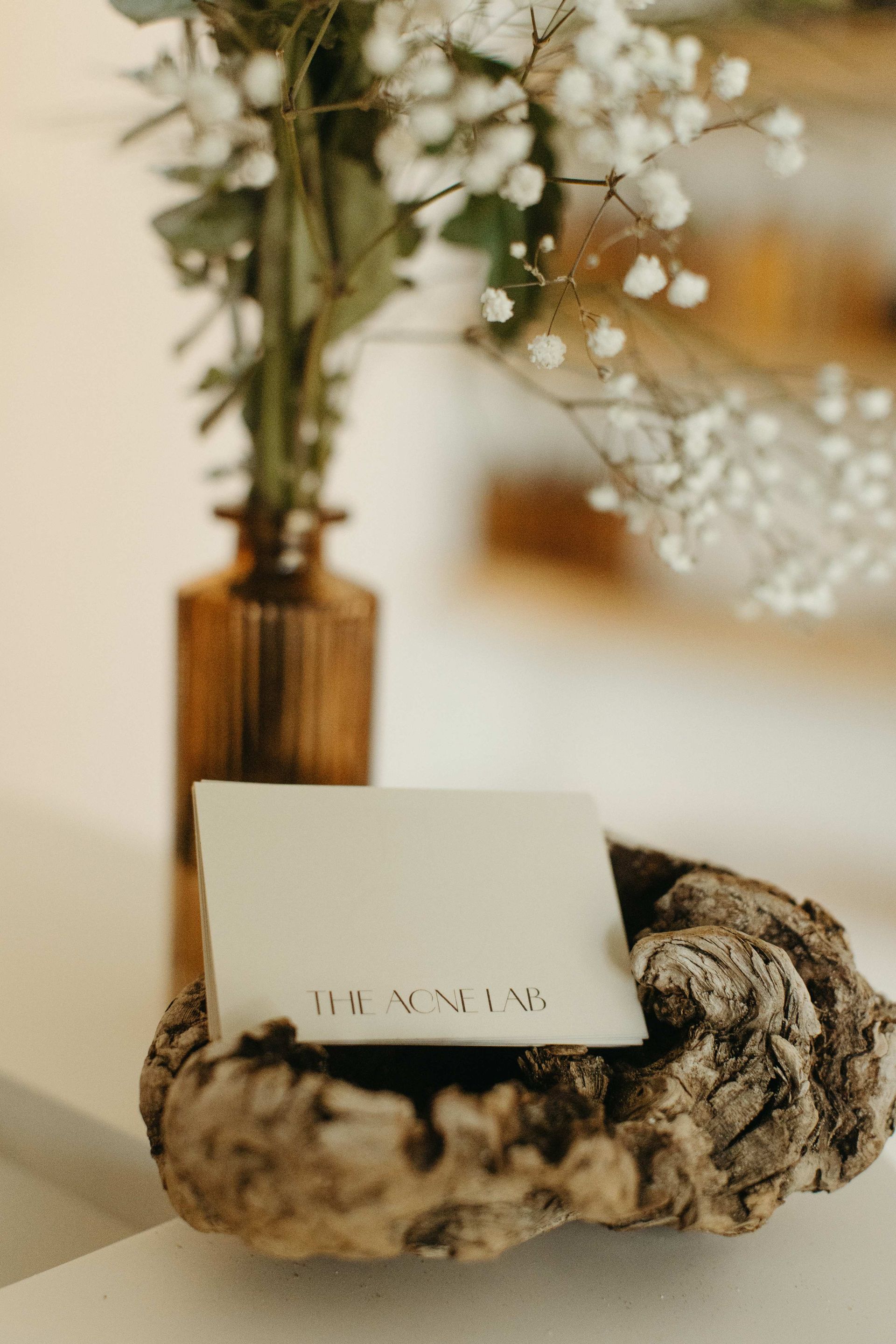 Name card with printed text sits on a weathered wood piece, with a vase of flowers in the background.