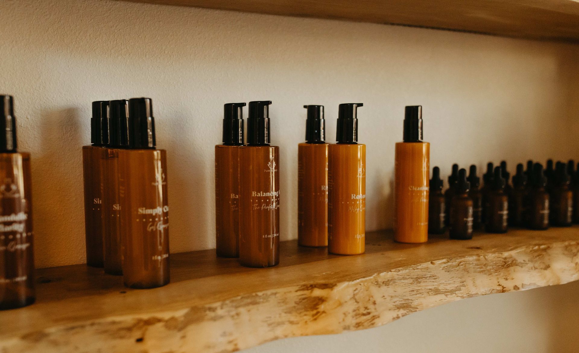 Bottles of skincare products on a wooden shelf. Various sizes and colors, all with dark lids.