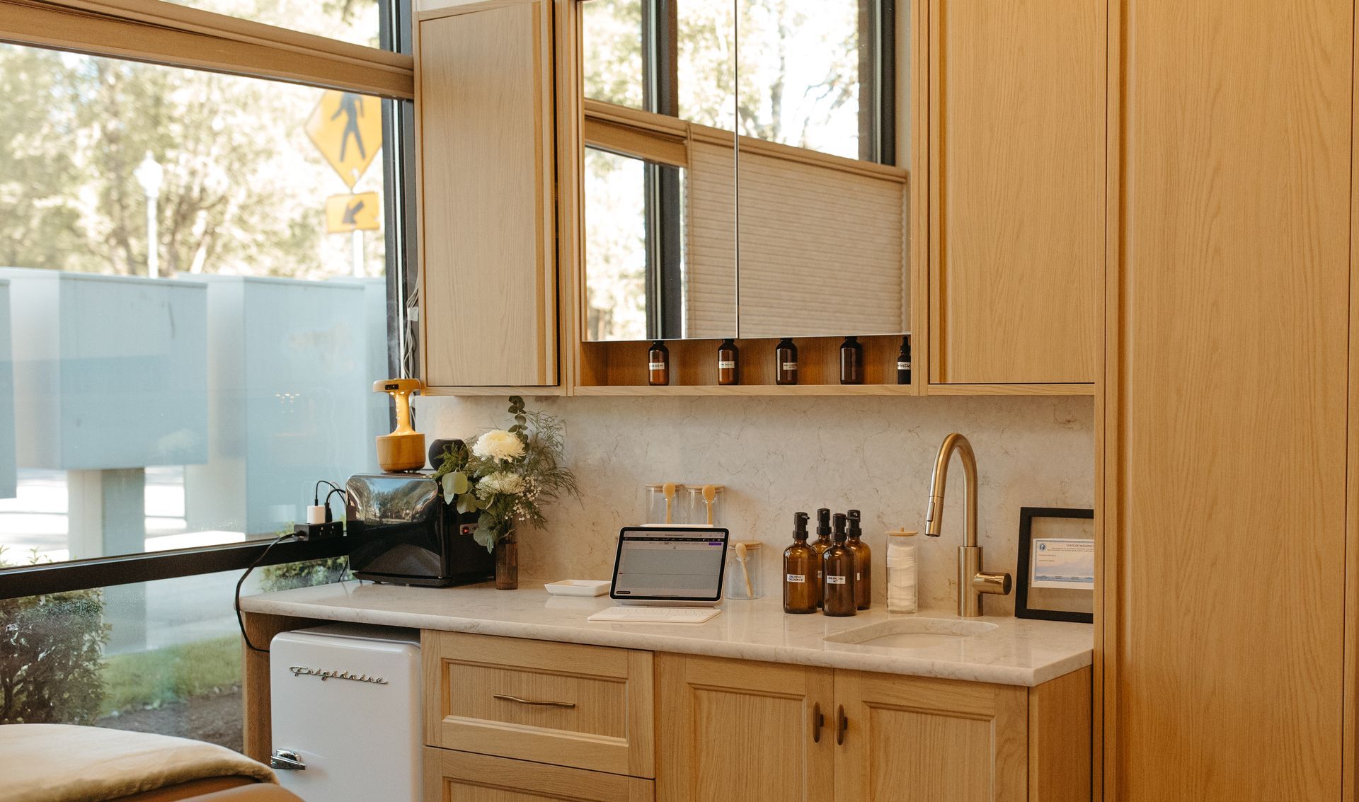 A spa treatment room with wood cabinets, a marble countertop, and a window overlooking the outdoors.