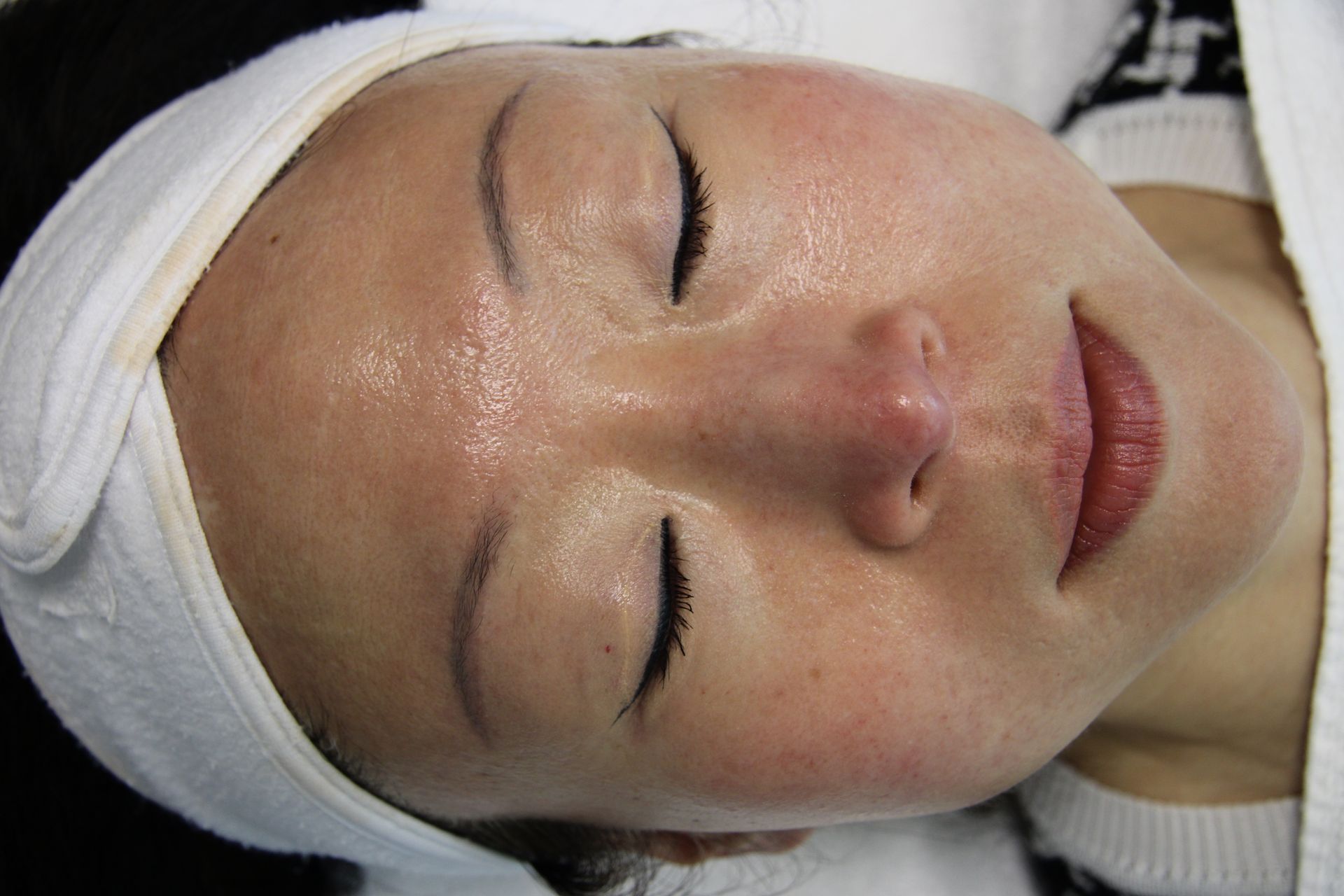 A woman is laying down with her eyes closed and a towel on her head.