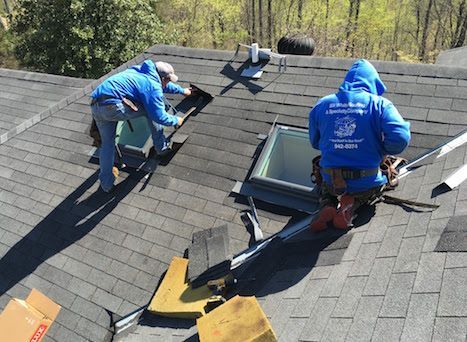 Two men are working on a roof with a skylight.