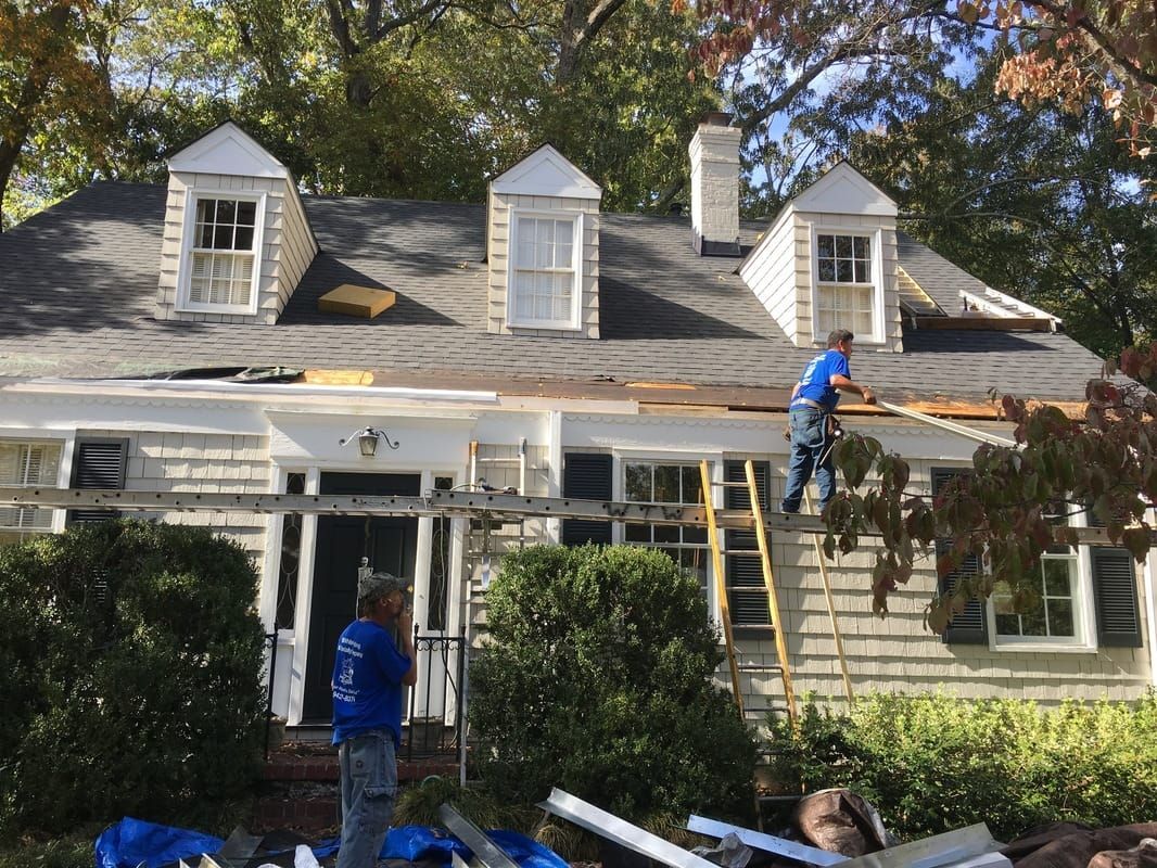 A man on a ladder is working on the roof of a house