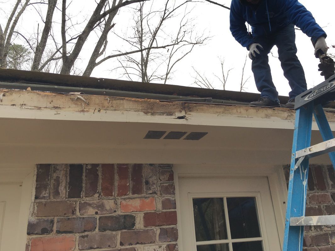 A man is standing on a ladder working on the roof of a house