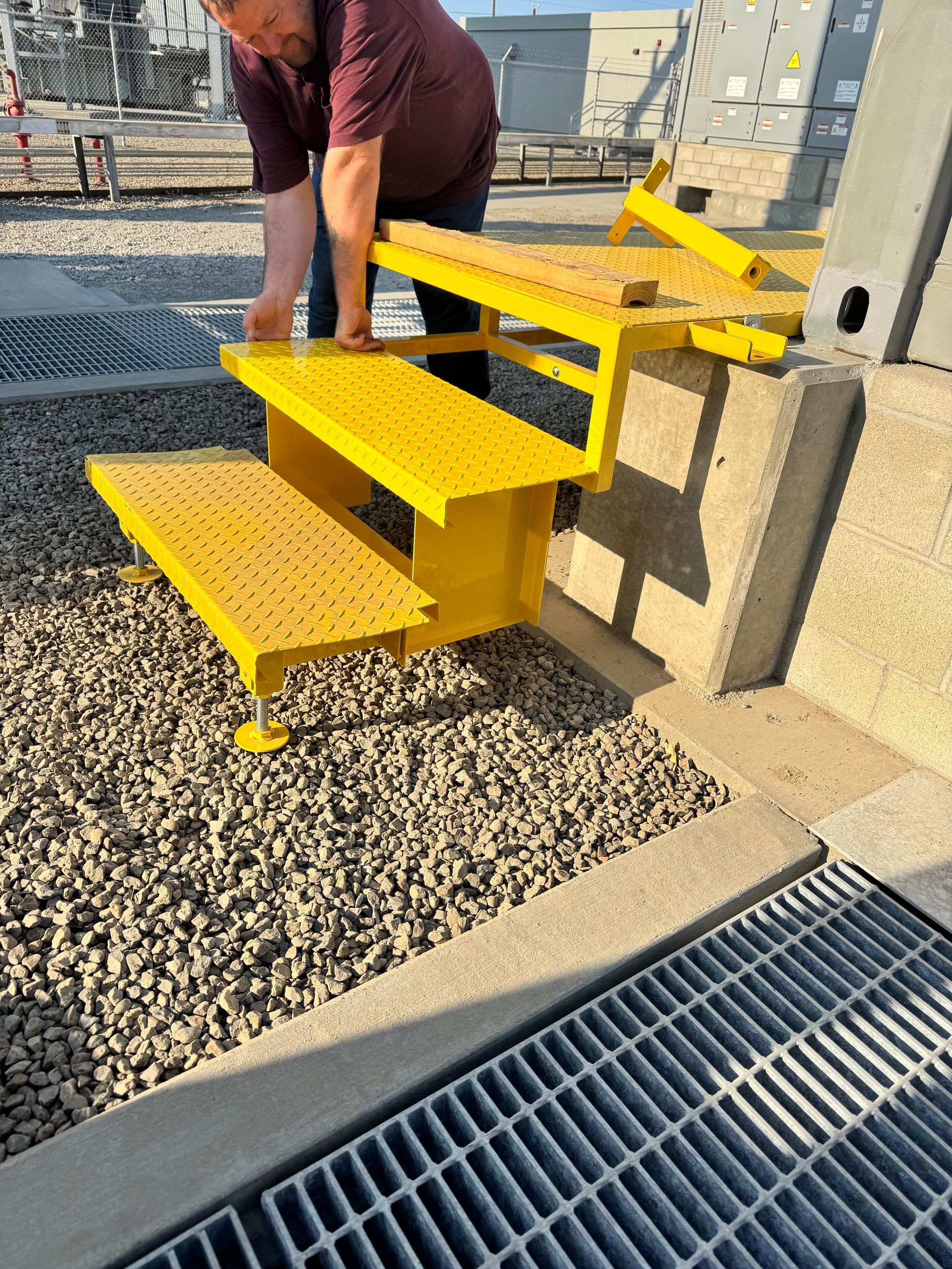 A person adjusts bright yellow metal steps near a concrete wall and a metal grate outdoors.