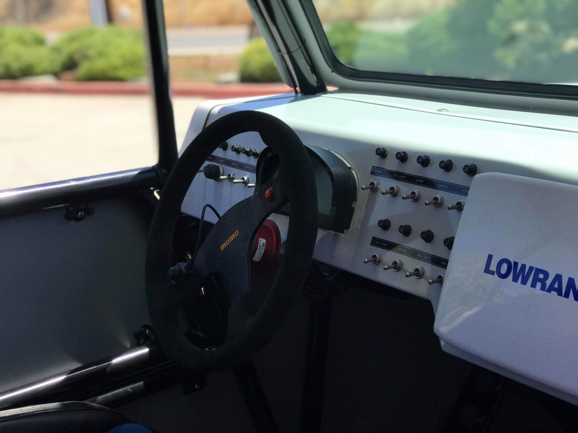 Interior of a race car. Black steering wheel, switches on dashboard, Lowrance screen, roll cage.