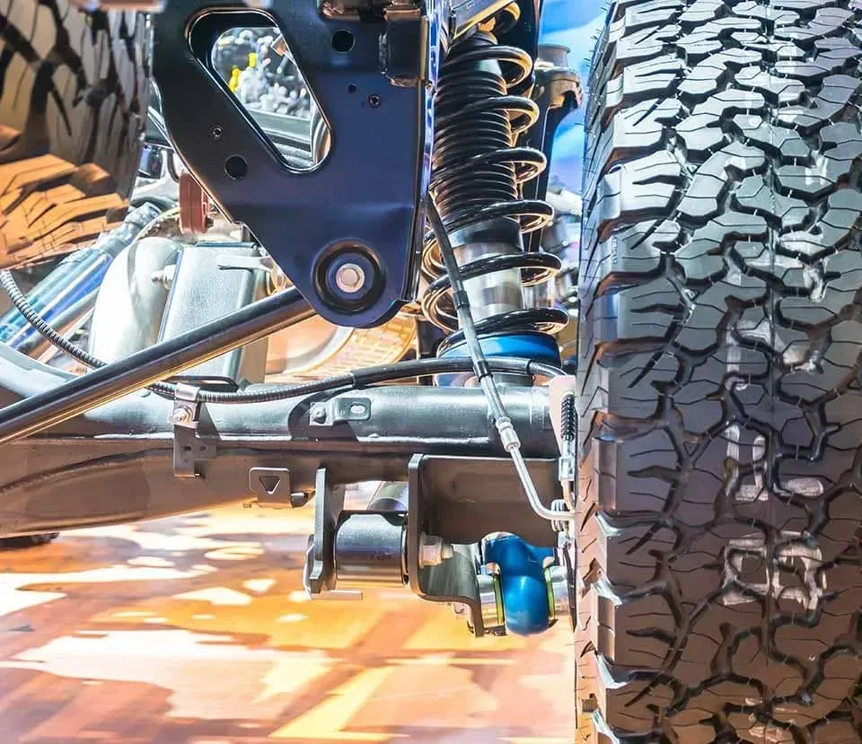 A close up of a suspension system on a truck with a tire in the background.