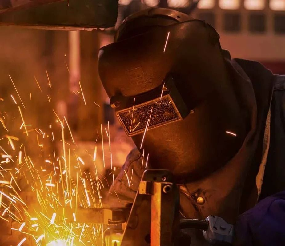 A man wearing a welding helmet is welding a piece of metal.