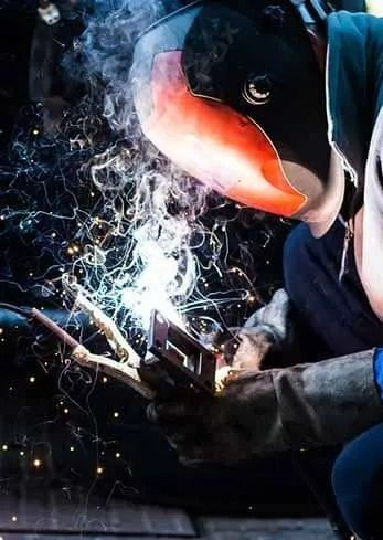 A man wearing a welding mask is welding a piece of metal.