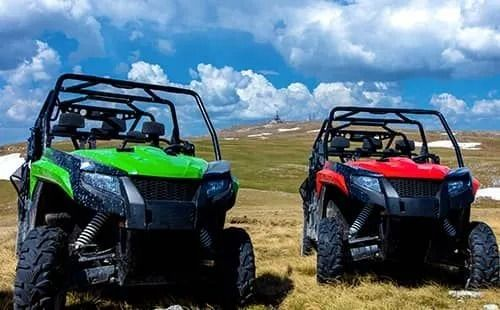 Two atvs are parked next to each other in a grassy field.