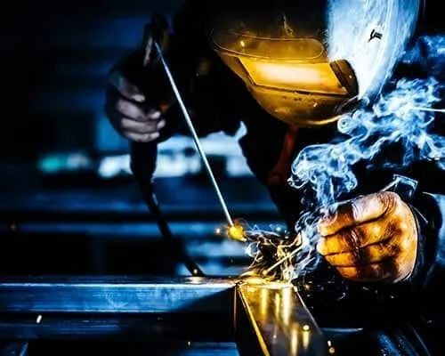 A man is welding a piece of metal with smoke coming out of his mouth.