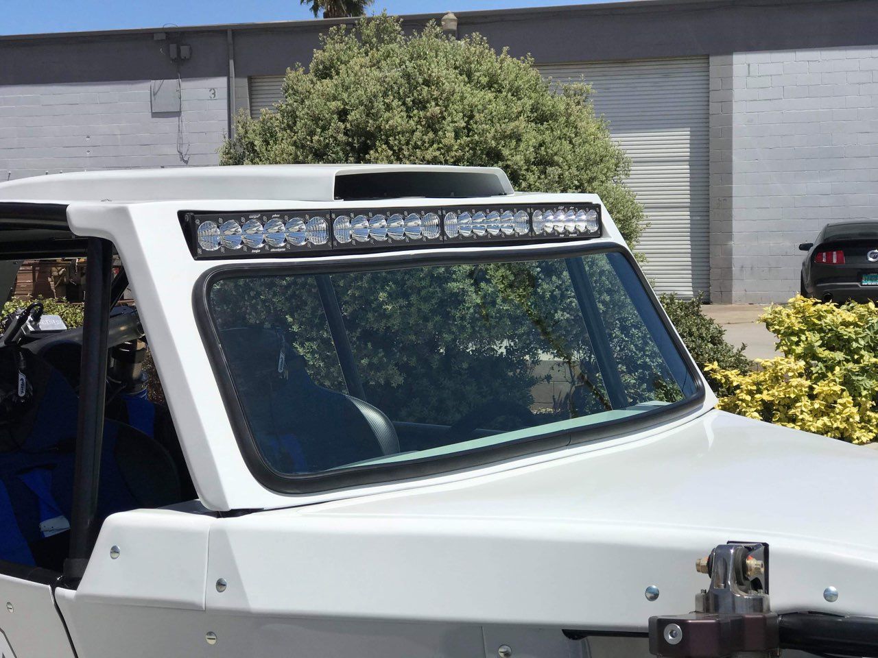 White off-road vehicle with a roof-mounted LED light bar, parked outdoors.