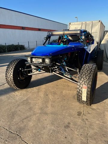 Blue and white off-road racing vehicle parked outdoors. Large tires, roll cage, and light bar.
