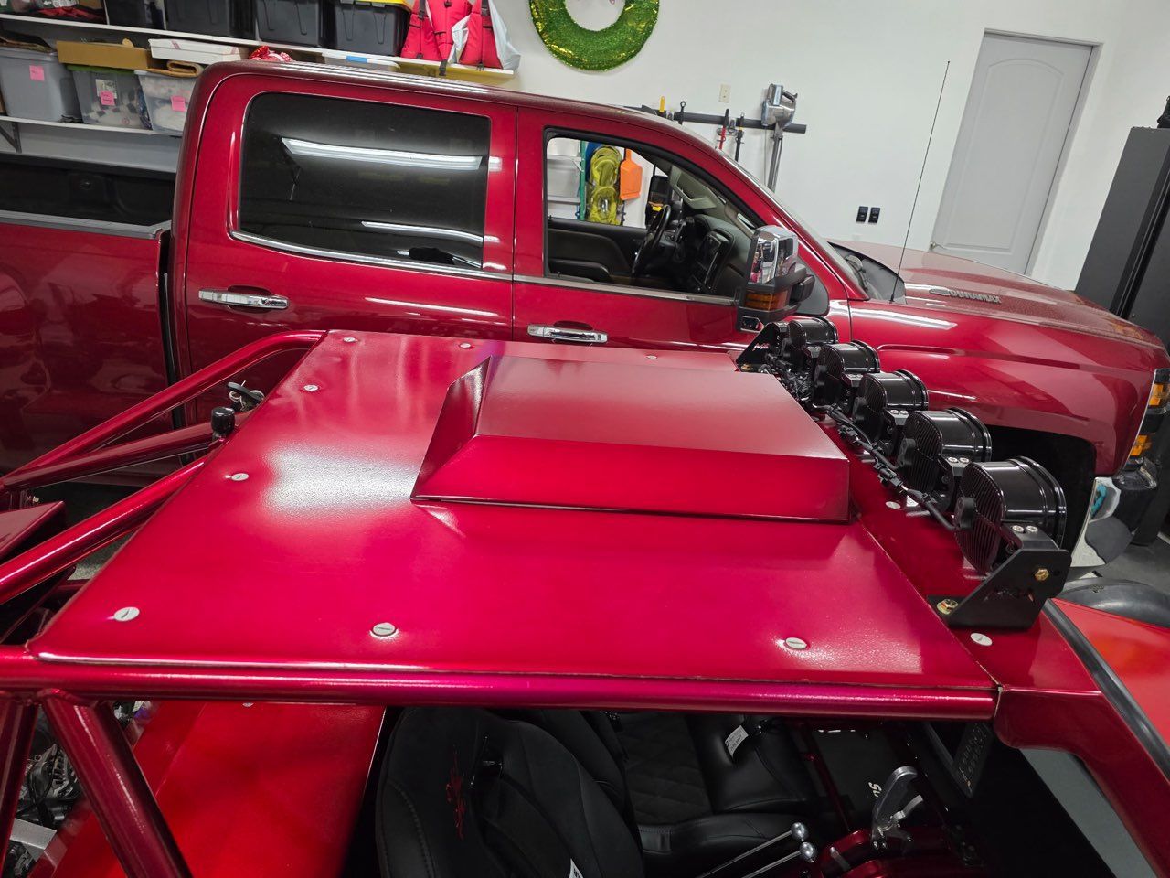 Red off-road vehicle with a custom roof, parked in a garage next to a red pickup truck.