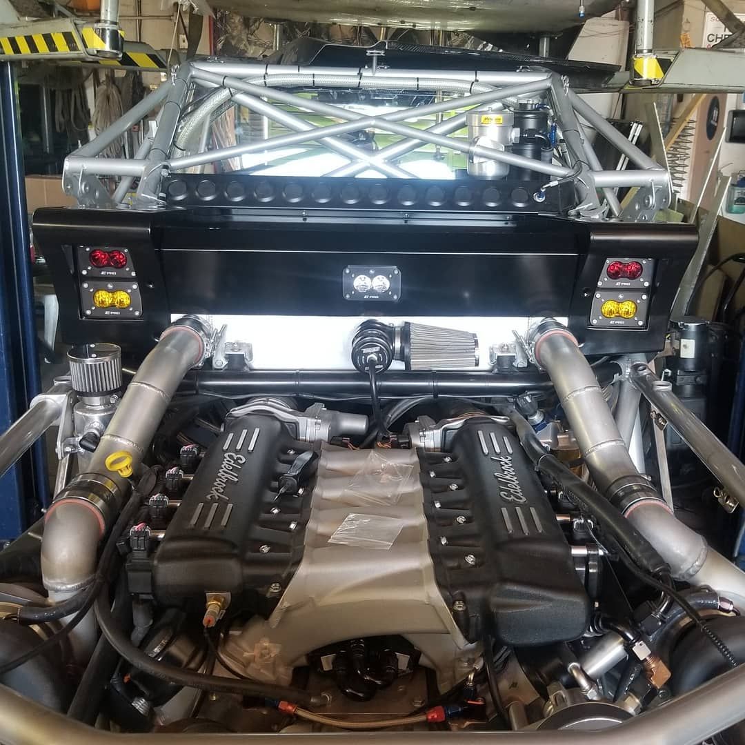 Engine bay of a black vehicle with two large engines, metal frame, and exhaust pipes.