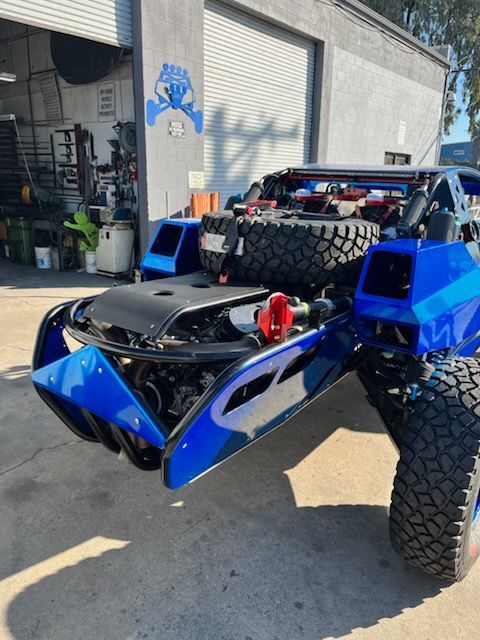 Blue off-road vehicle parked outside a garage, with large tires and angular bodywork.