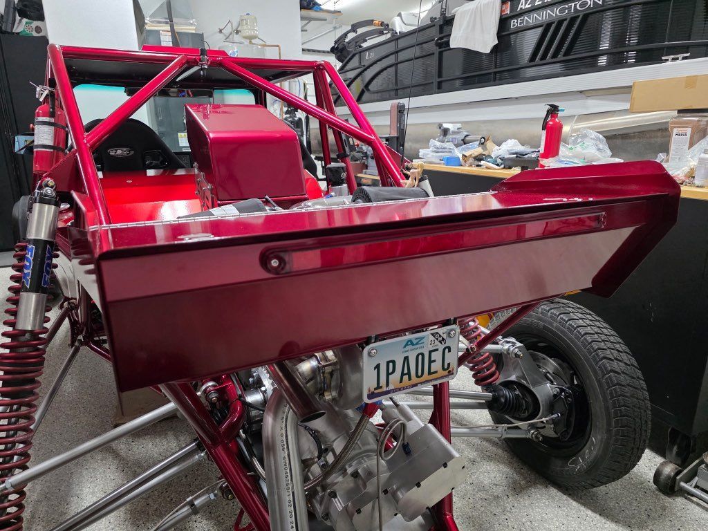 Red custom-built buggy with roll cage, license plate visible.