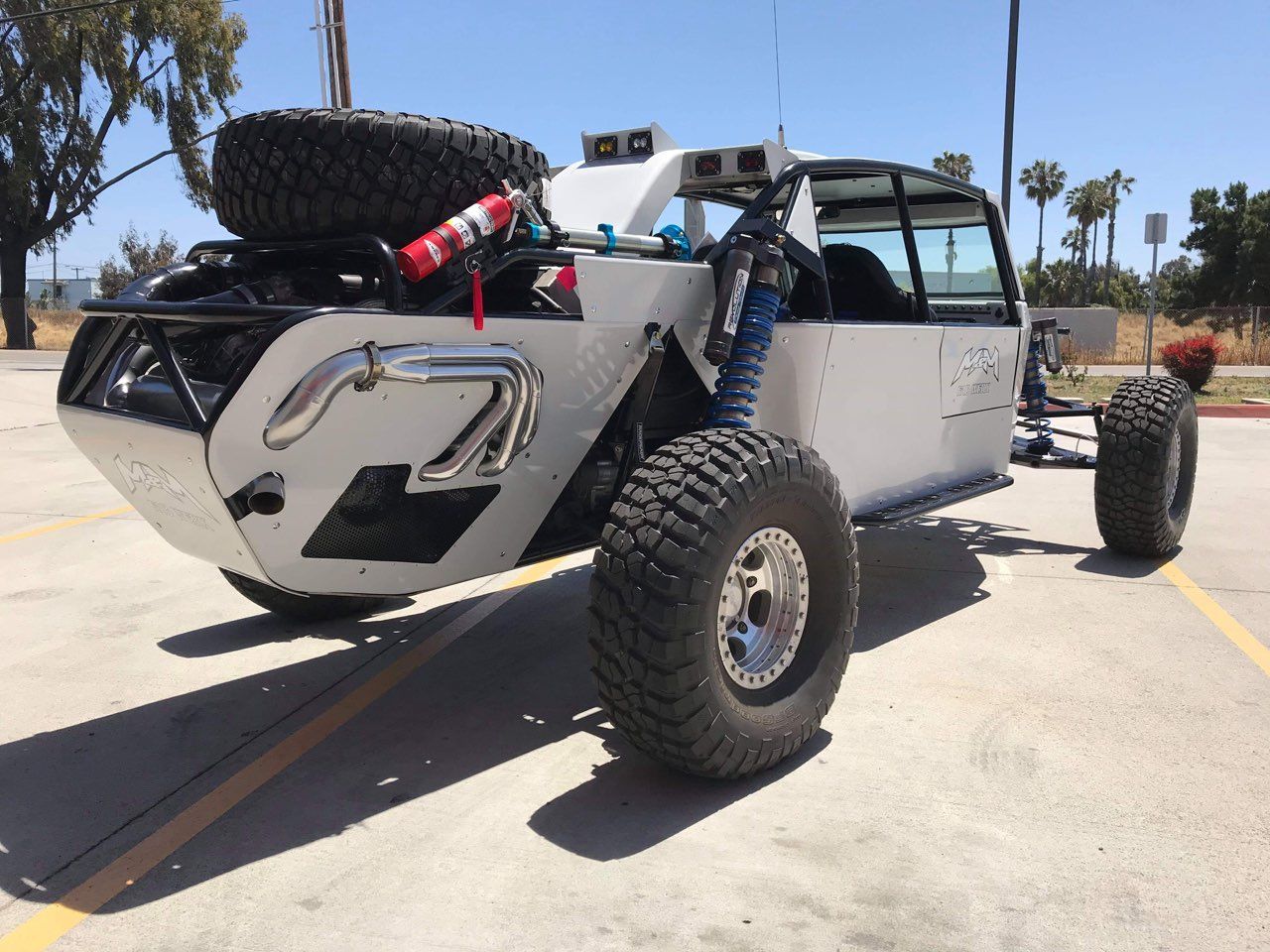 Off-road vehicle on pavement, gray body, large tires, spare tire on rear, fire extinguisher.