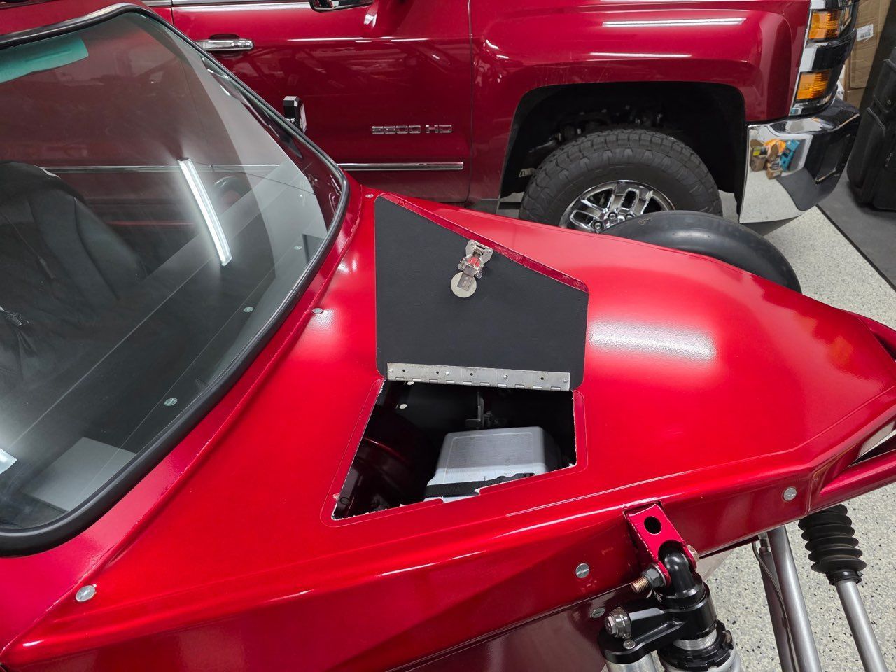 Red custom car hood with black vent. A red truck is in the background.