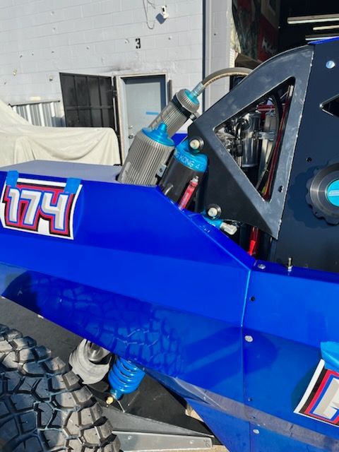 Blue off-road vehicle with the number 174. Shock absorbers, suspension, and roll cage visible.