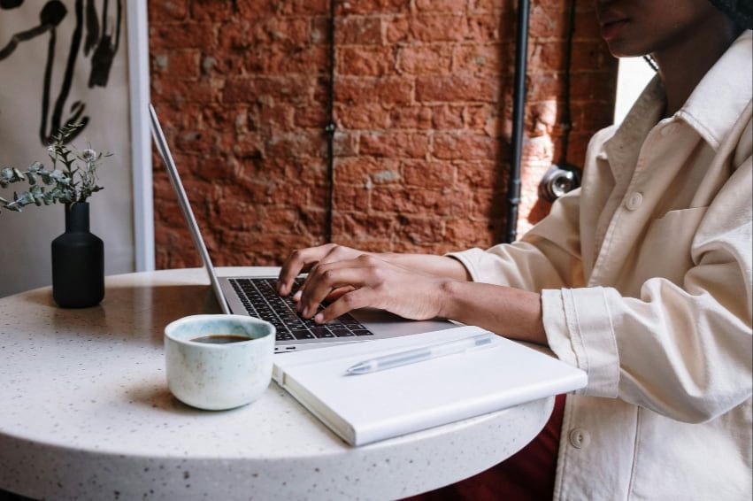 A woman is sitting at a table typing on a laptop computer.