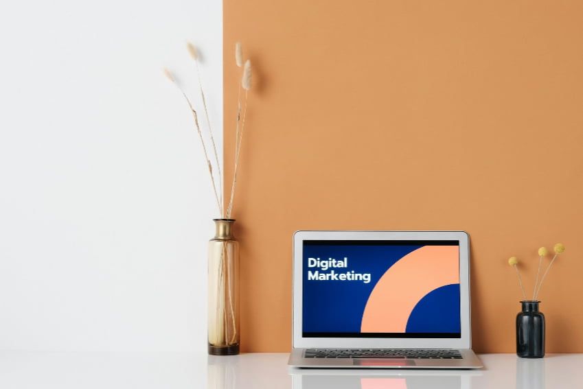 A laptop computer is sitting on a desk next to a vase of flowers.