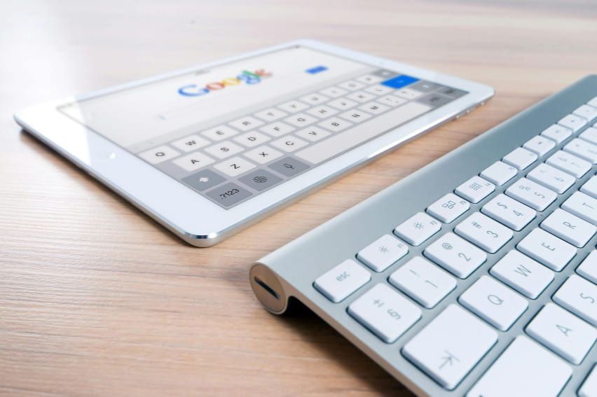 A keyboard and a tablet are on a wooden table.