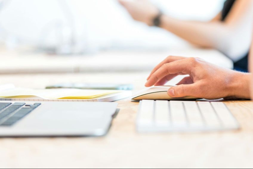 A person is typing on a computer mouse in front of a laptop.