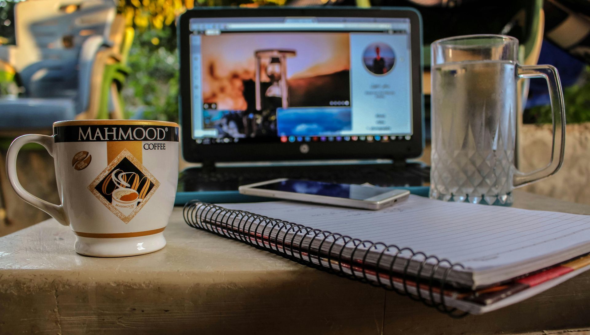 A cup of coffee is sitting on a table next to a laptop and a notebook.