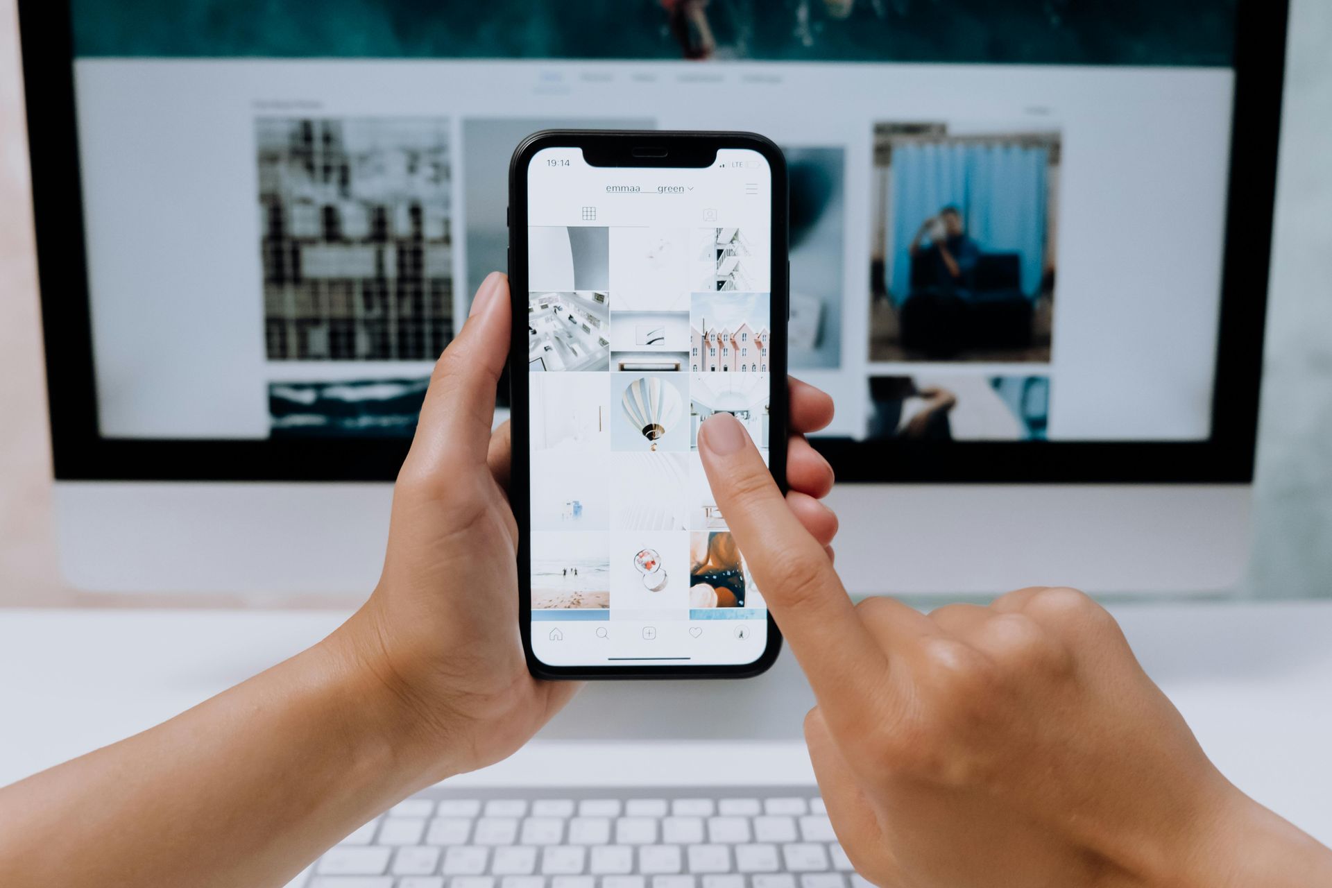 A person is holding a cell phone in front of a computer.