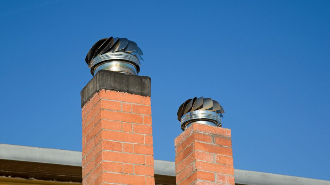Two brick chimneys with spinning metal vent caps against a clear blue sky.