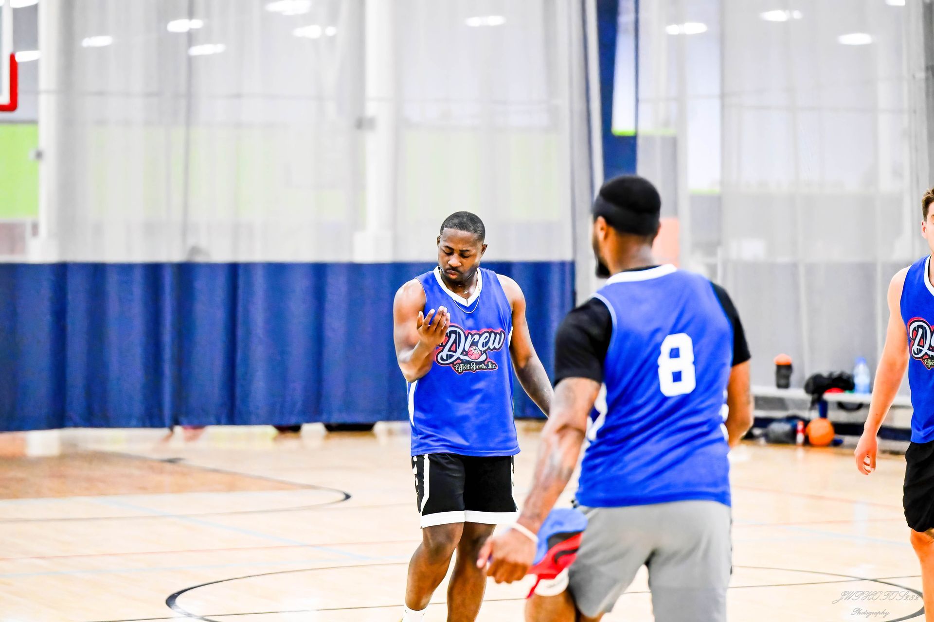 Three basketball players in blue jerseys on an indoor court, with one gesturing toward the ball.
