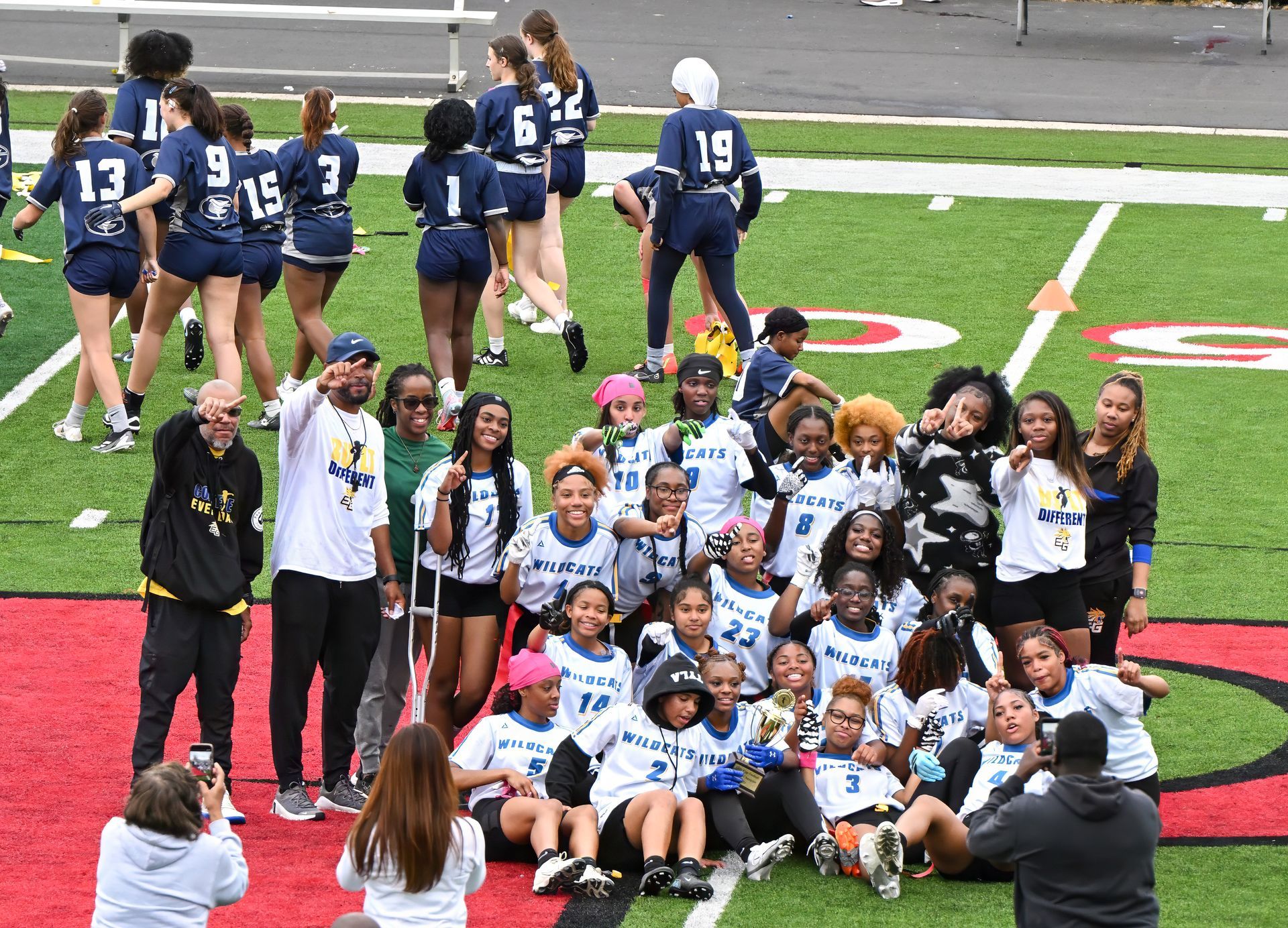 A large group of athletes in matching white jerseys poses for a photo on a green sports field with a red end zone.