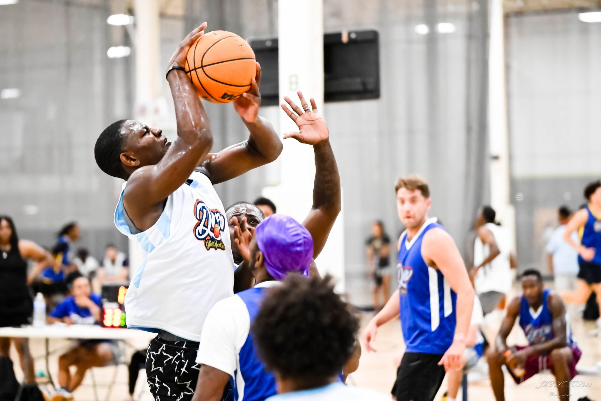 A basketball player in a white jersey goes up for a shot while being defended in an indoor court.