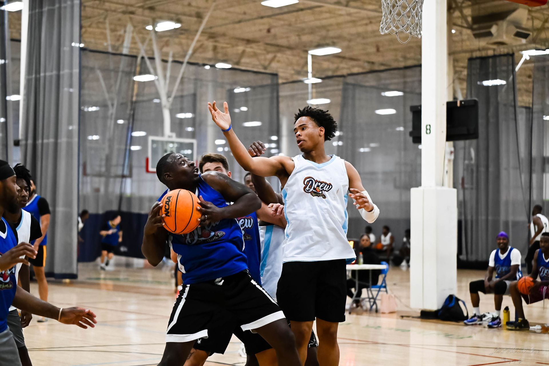 Players in blue and white jerseys compete for a basketball during an indoor game.