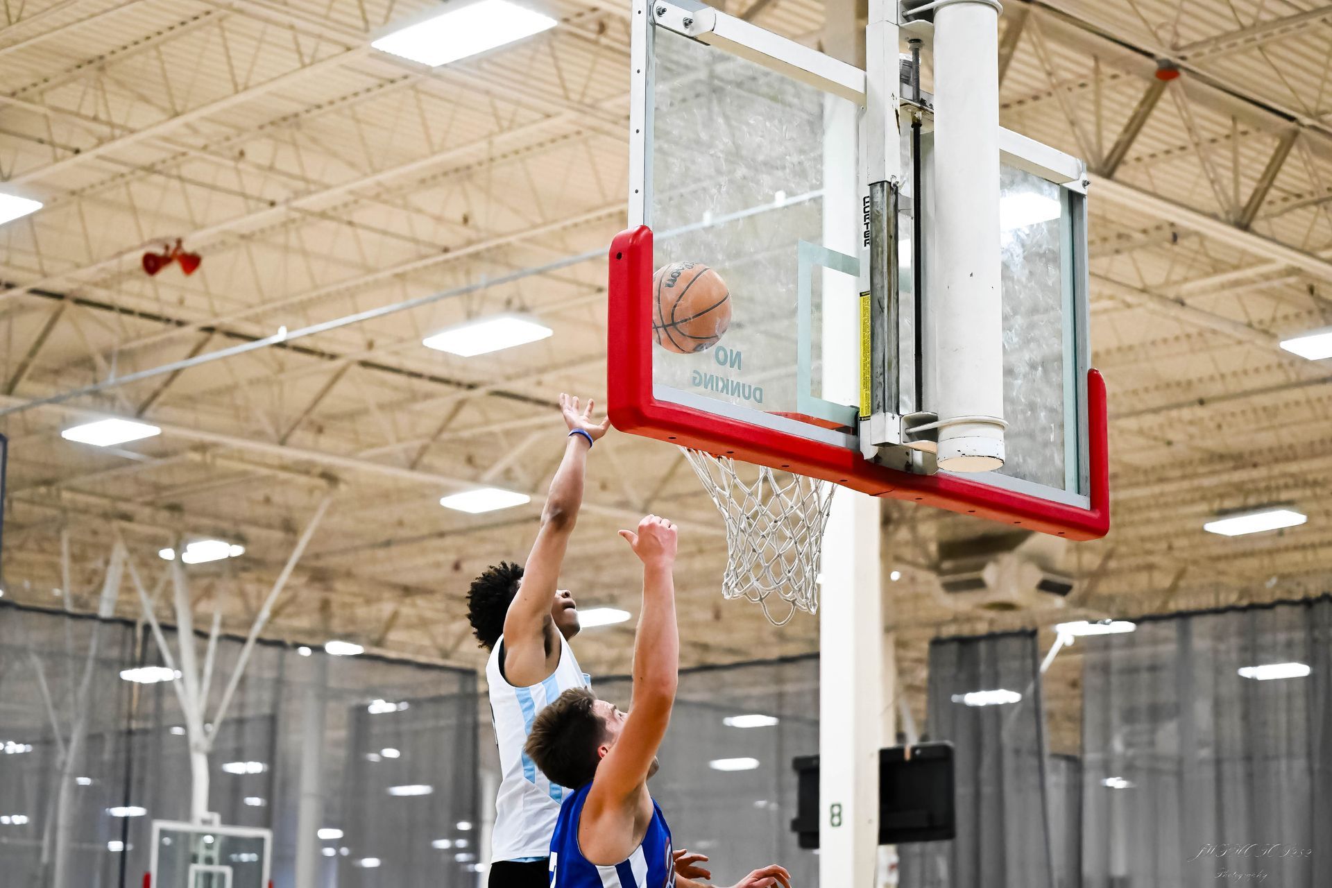 Two basketball players competing for a rebound near the hoop during an indoor game.