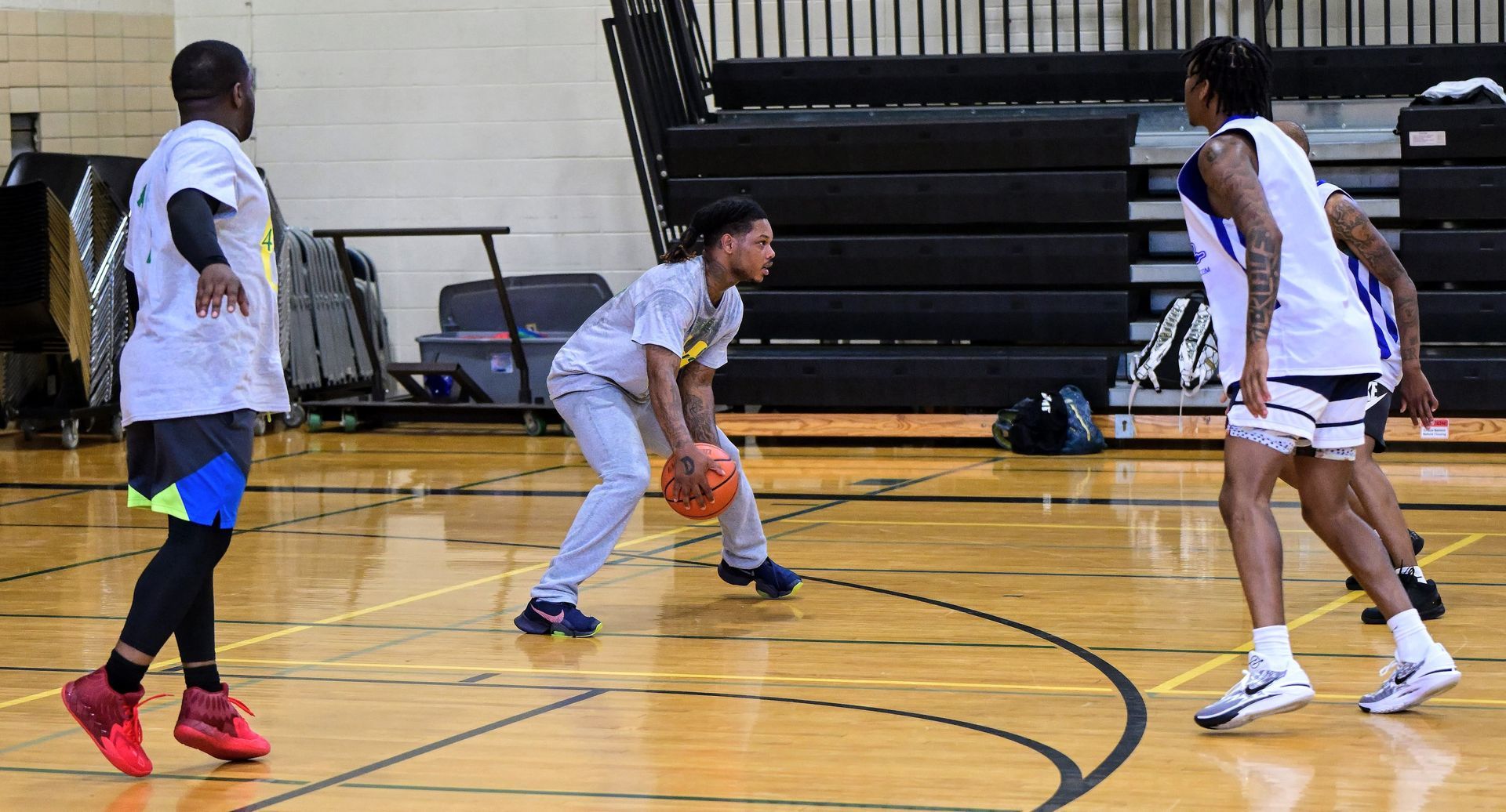 Three people practicing basketball on an indoor court, with one holding a ball in a low stance.
