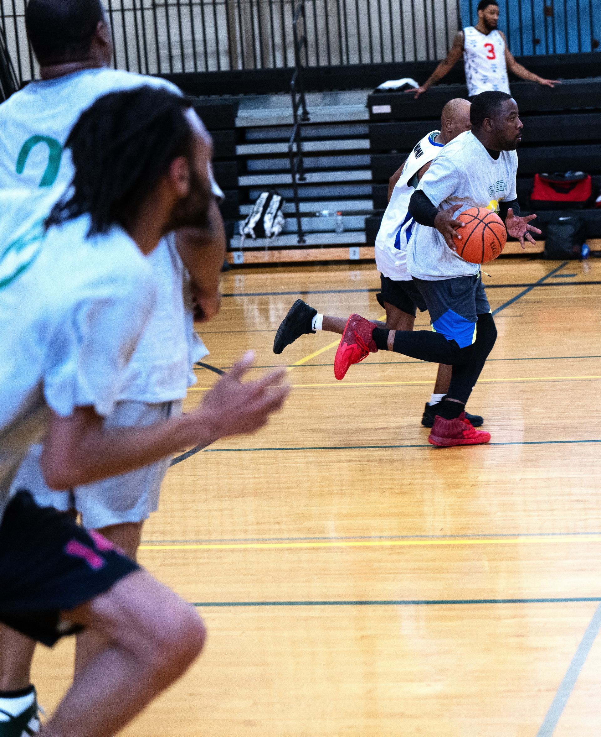 A basketball player in a white uniform dribbles on a hardwood court while others move alongside him.