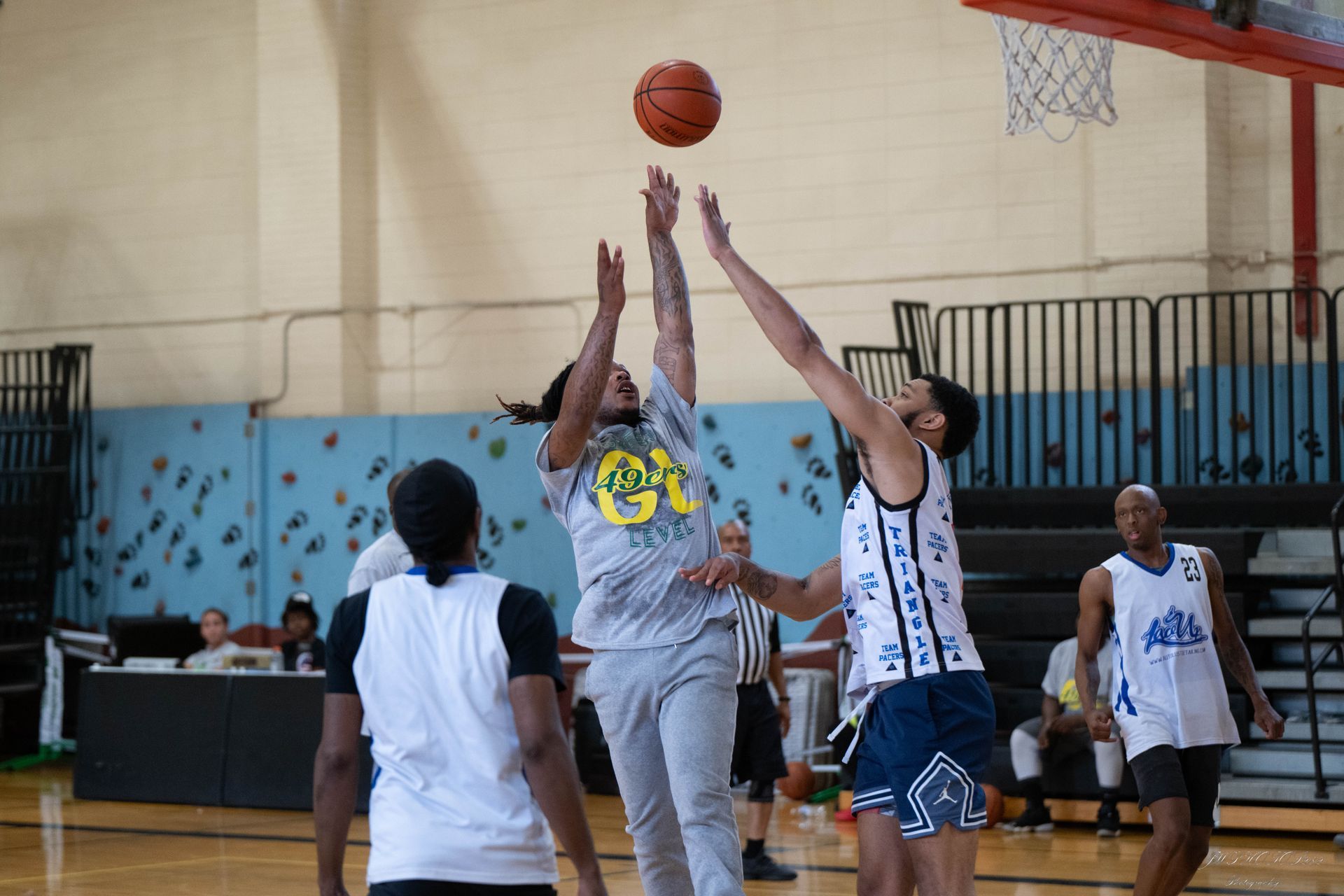 Two basketball players jump to reach a ball mid-air during a game in a gymnasium.