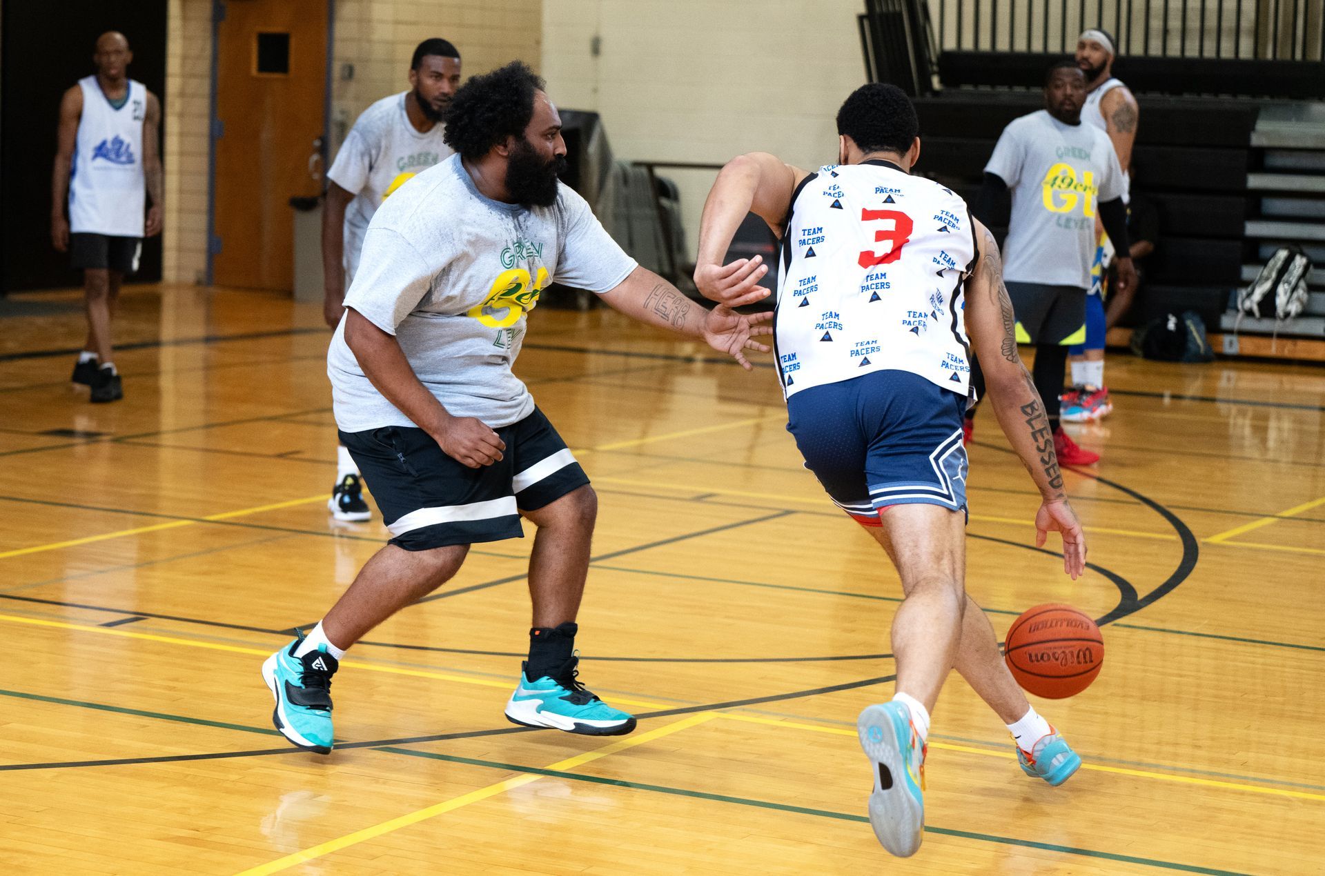 A person dribbling a basketball past a defender on an indoor wood court.