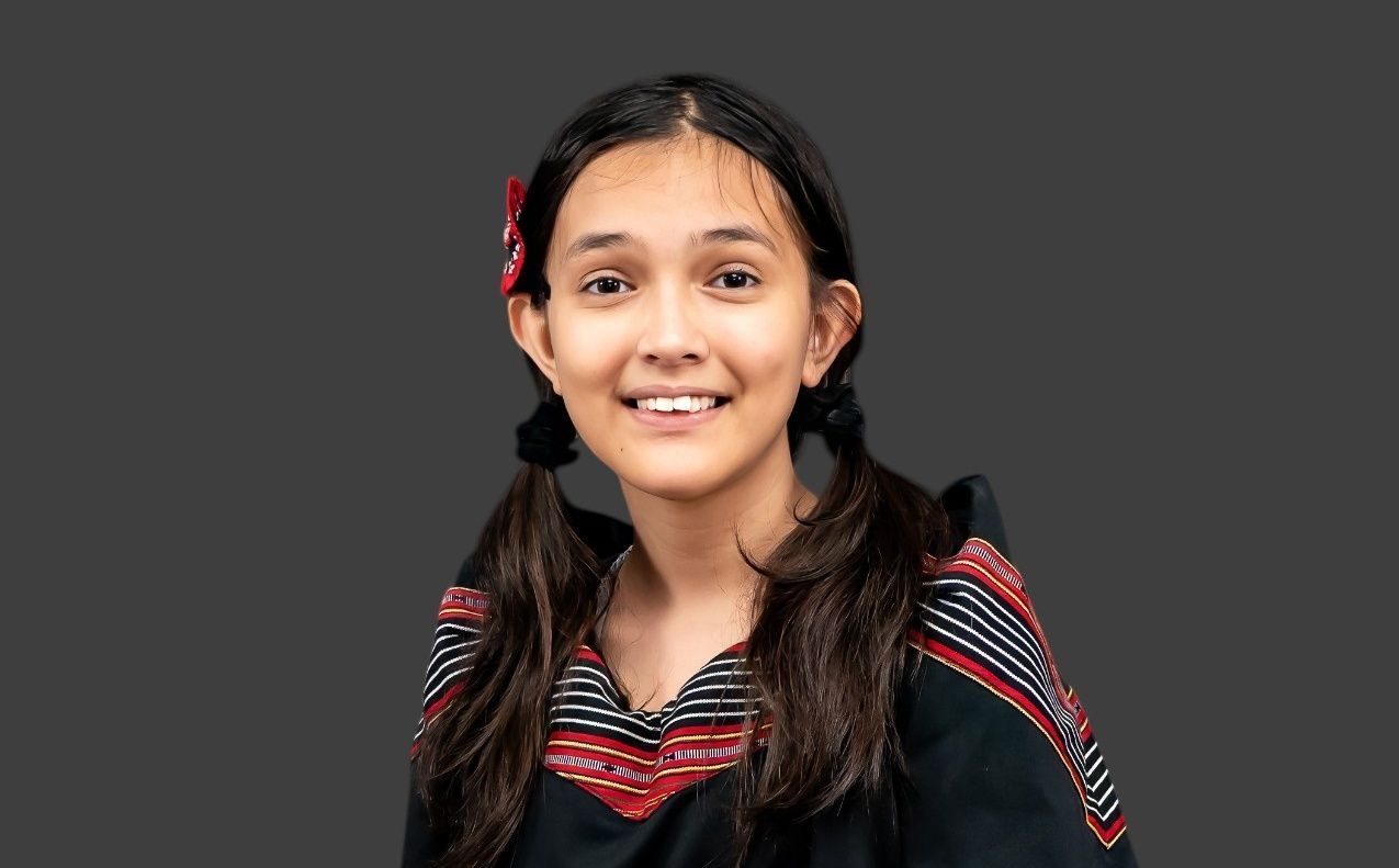 A smiling person with dark hair in pigtails wearing a black top with red and white striped patterns against a gray backdrop.